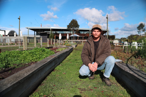 A man kneeling between garden beds on a farm