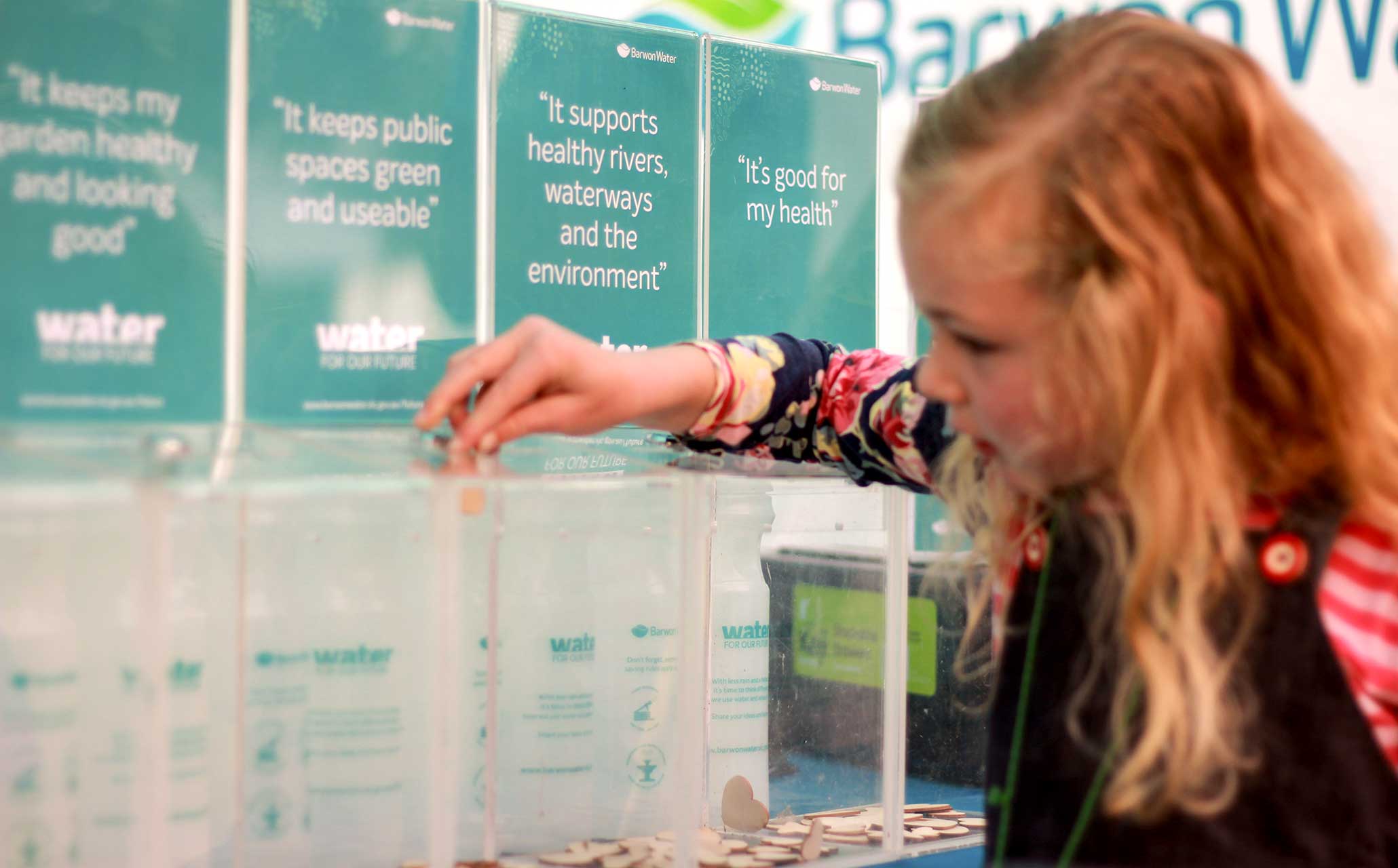 Photo of young girl placing a wooden counter in a clear plastic box at a Water for Our Future pop-up stand.