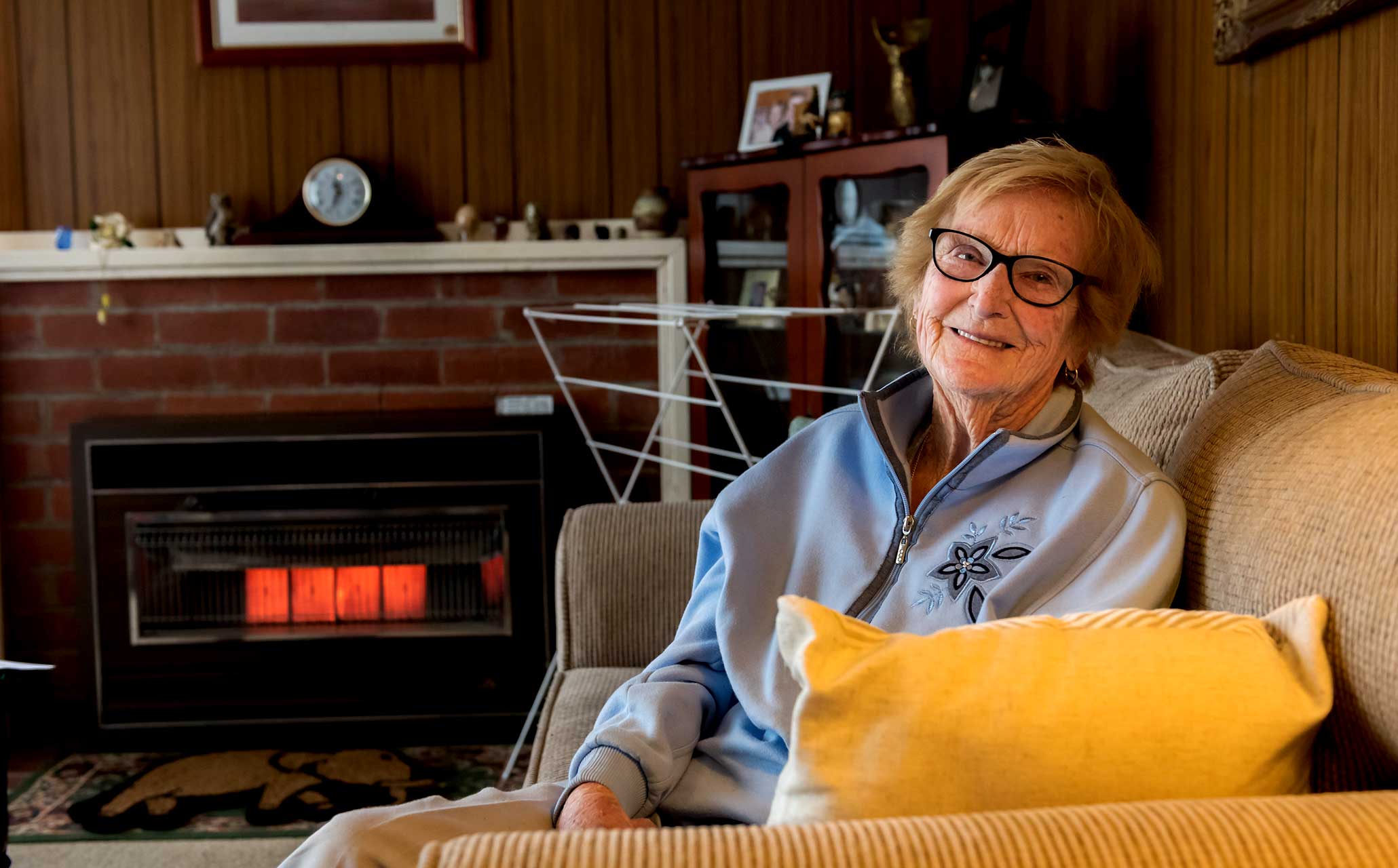 Photo of elderly lady sitting on our couch in her home with the heater going in the background.
